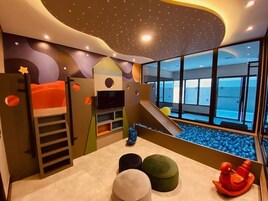 Um espaço de brincadeiras infantil com beliches, um escorrega e uma piscina de bolinhas.