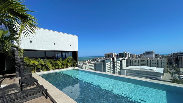 A rooftop pool with a city view, surrounded by palm trees and modern buildings. - Sky Concept 816 (Maceió)