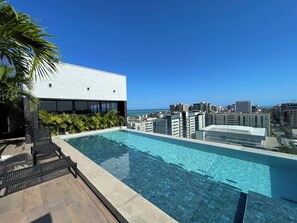 Piscina en la azotea con vista a la ciudad, rodeada de palmeras y edificios modernos.