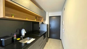 A modern kitchen with black countertops, a sink, and a refrigerator. There is a wooden shelf above the counter with small plants. - Sky Concept 816 (Maceió)