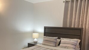 Una cama bien hecha con una colcha a rayas, una lámpara de noche y una cortina en la ventana.