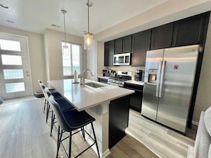 A modern kitchen with a central island, stainless steel appliances, and a dining area with bar stools.