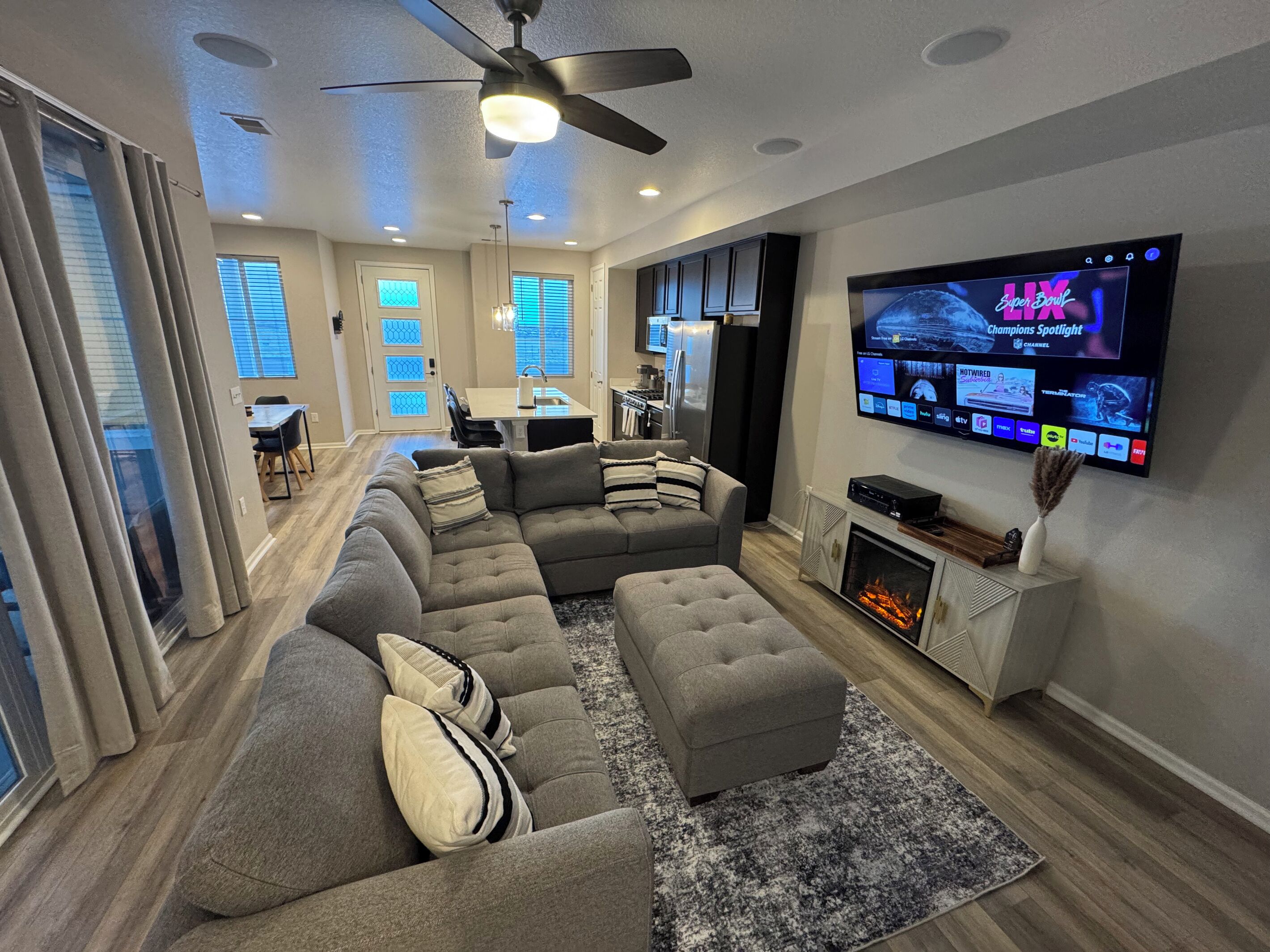 Un salon moderne avec un canapé d’angle, une cheminée et un téléviseur à écran plat diffusant le Super Bowl.
