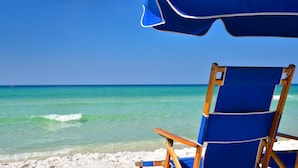 A beach scene with a blue beach chair and an umbrella, clear turquoise water, and a sandy beach. - Surfside Resort #404 (Miramar Beach)