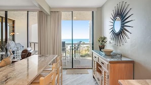 A modern kitchen with a large island, a dining area with a view of the ocean, and a decorative mirror on the wall. - Surfside Resort #404 (Miramar Beach)