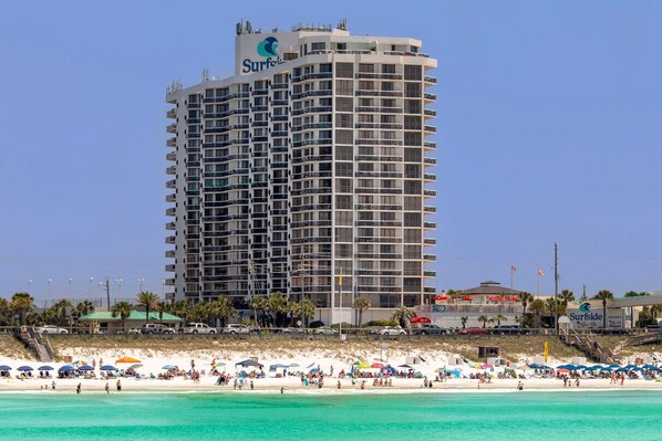 A high-rise hotel with multiple balconies, a beach in the foreground, and a clear blue sky. - Surfside Resort #404 (Miramar Beach)