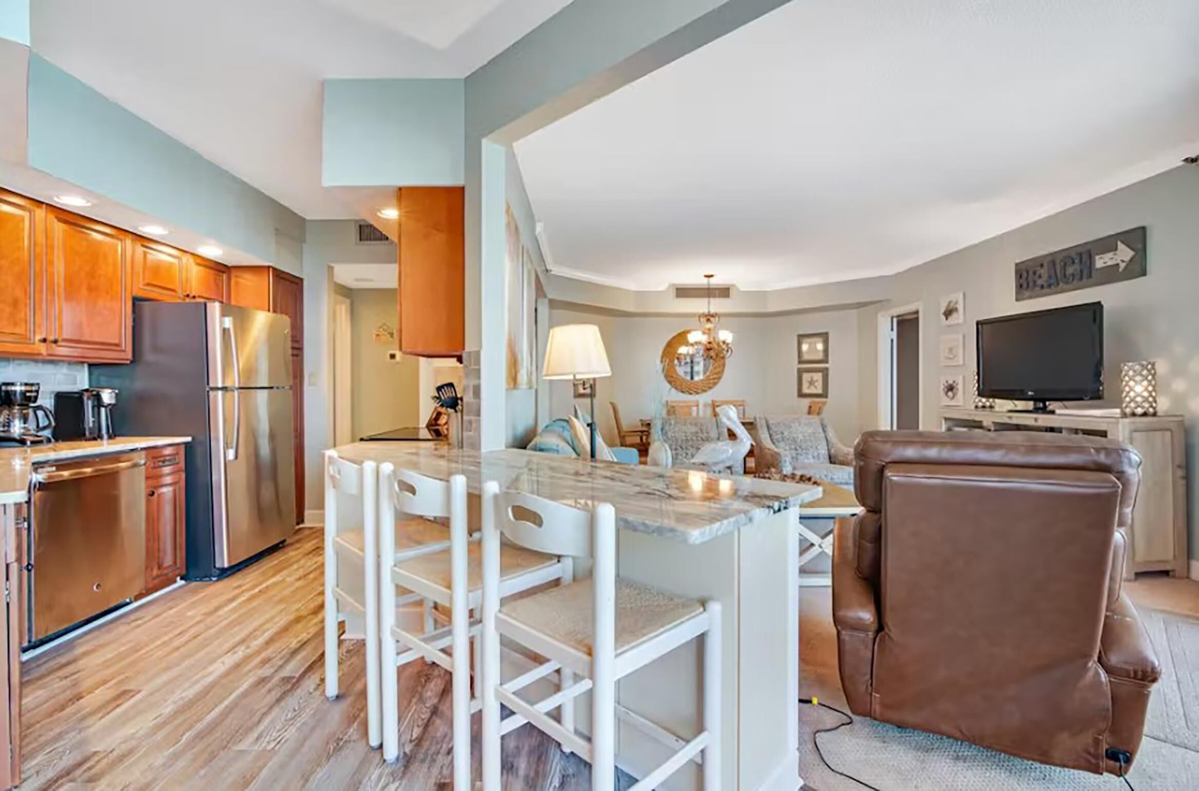 A modern kitchen with wooden cabinets, a stainless steel refrigerator, and a marble island with bar stools.