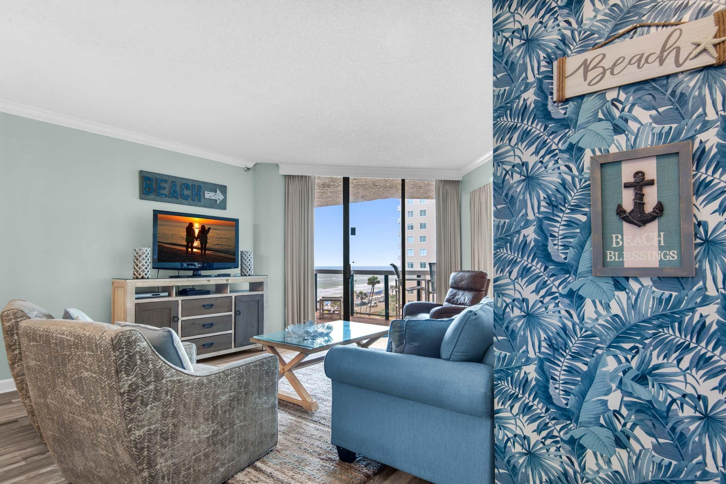 A living room with a television, a sofa, a coffee table, and a view of the ocean.