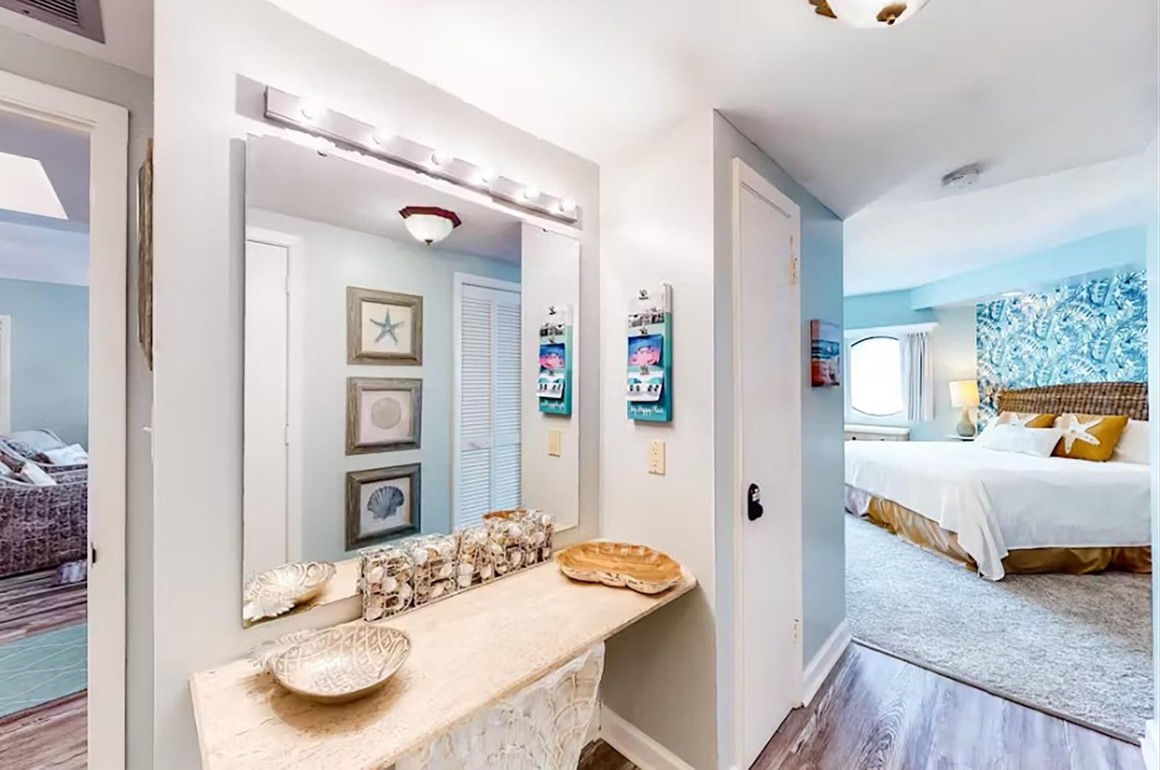 A hallway with a vanity, a bed with a white and gold bedspread, and a wall with framed pictures and a tapestry.