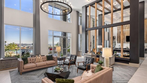 A spacious living area with a high ceiling, large windows, and a modern kitchen in the background. - Landing | Amazing 2BD, Pool, Clubhouse (Park Hills)