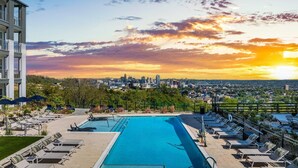 A rooftop pool with lounge chairs and a city skyline view at sunset. - Landing | Amazing 2BD, Pool, Clubhouse (Park Hills)