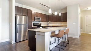 Una cocina moderna con electrodomésticos de acero inoxidable, armarios de madera oscura, encimera de granito y una zona de asientos con taburetes de bar.