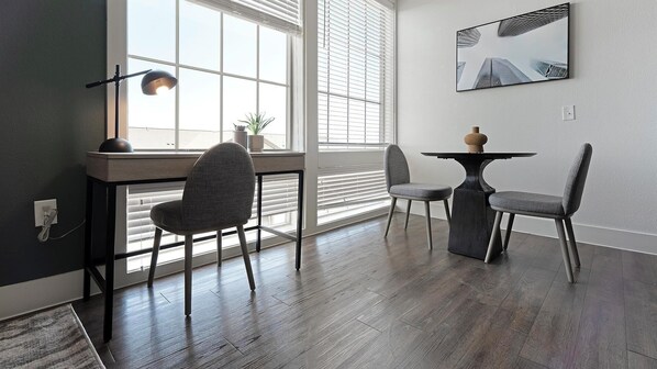 A modern dining area with a wooden table and two chairs, a potted plant, and a cityscape painting on the wall.