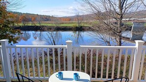 Una terraza con una mesa y sillas con vista a un lago rodeado de follaje otoñal.