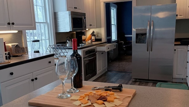 Una cocina moderna con armarios blancos, electrodomésticos de acero inoxidable y una encimera de madera con copas de queso y vino.