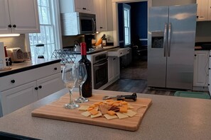 A modern kitchen with white cabinets, stainless steel appliances, and a wooden countertop with cheese and wine glasses.