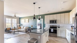 A modern kitchen with stainless steel appliances, a dining area with a round table, and a living room with a sofa and a coffee table. - Landing | Incredible 2BD, Pool, Yoga Studio (Florence)
