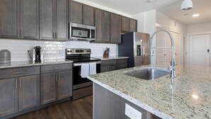A modern kitchen with dark wood cabinets, stainless steel appliances, granite countertops, and a stainless steel sink.