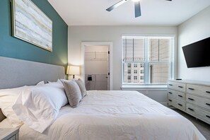 Een slaapkamer met een groot bed, een aan de muur bevestigde televisie en een raam met zonwering.