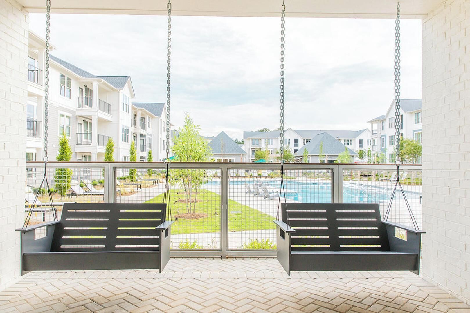 Ein Balkon mit zwei Schaukeln mit Blick auf einen Swimmingpool und Wohnhäuser.