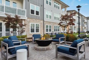 A courtyard with outdoor seating, a fire pit, and a stone building with multiple windows and balconies. - Landing | Beautiful 2BD, Pool, Game Room (Matthews)