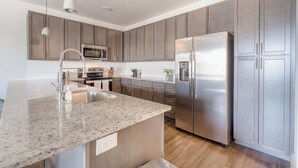 Une cuisine moderne dotée de plans de travail en granit, d’appareils électroménagers en acier inoxydable et d’armoires en bois.