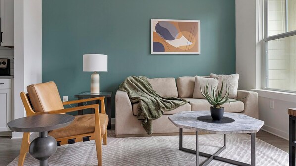 Ein modernes Wohnzimmer mit einer türkisfarbenen Wand, einem beigen Sofa, einem Holzstuhl, einem kleinen Tisch und einer Topfpflanze.