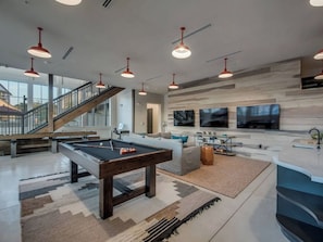 A spacious living area with a pool table, comfortable seating, a staircase, and a large TV wall. - Landing | Modern 1BD, Clubhouse, Gym (San Antonio)