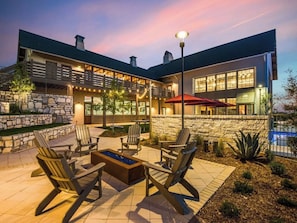 A modern building with a stone facade, outdoor seating area with chairs and a fire pit, and a pool in the background. - Landing | Modern 1BD, Clubhouse, Gym (San Antonio)