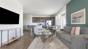 Ein modernes Wohnzimmer mit einem grauen Sofa, einem Glastisch und einem wandmontierten Flachbildfernseher.