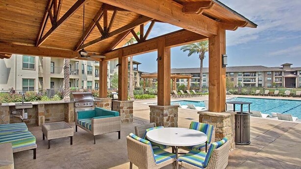 Un espacio al aire libre techado con muebles de mimbre, una parrilla y una piscina.