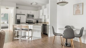 A modern kitchen with white cabinets, stainless steel appliances, and a central island with bar stools. - Landing | Stunning 2BD, Yoga Studio, Tennis Court (Atlanta)