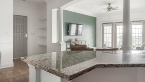 A spacious kitchen with a granite countertop, a dining area with a table and chairs, and a large window providing natural light. - Landing | Stunning 2BD, Yoga Studio, Tennis Court (Atlanta)