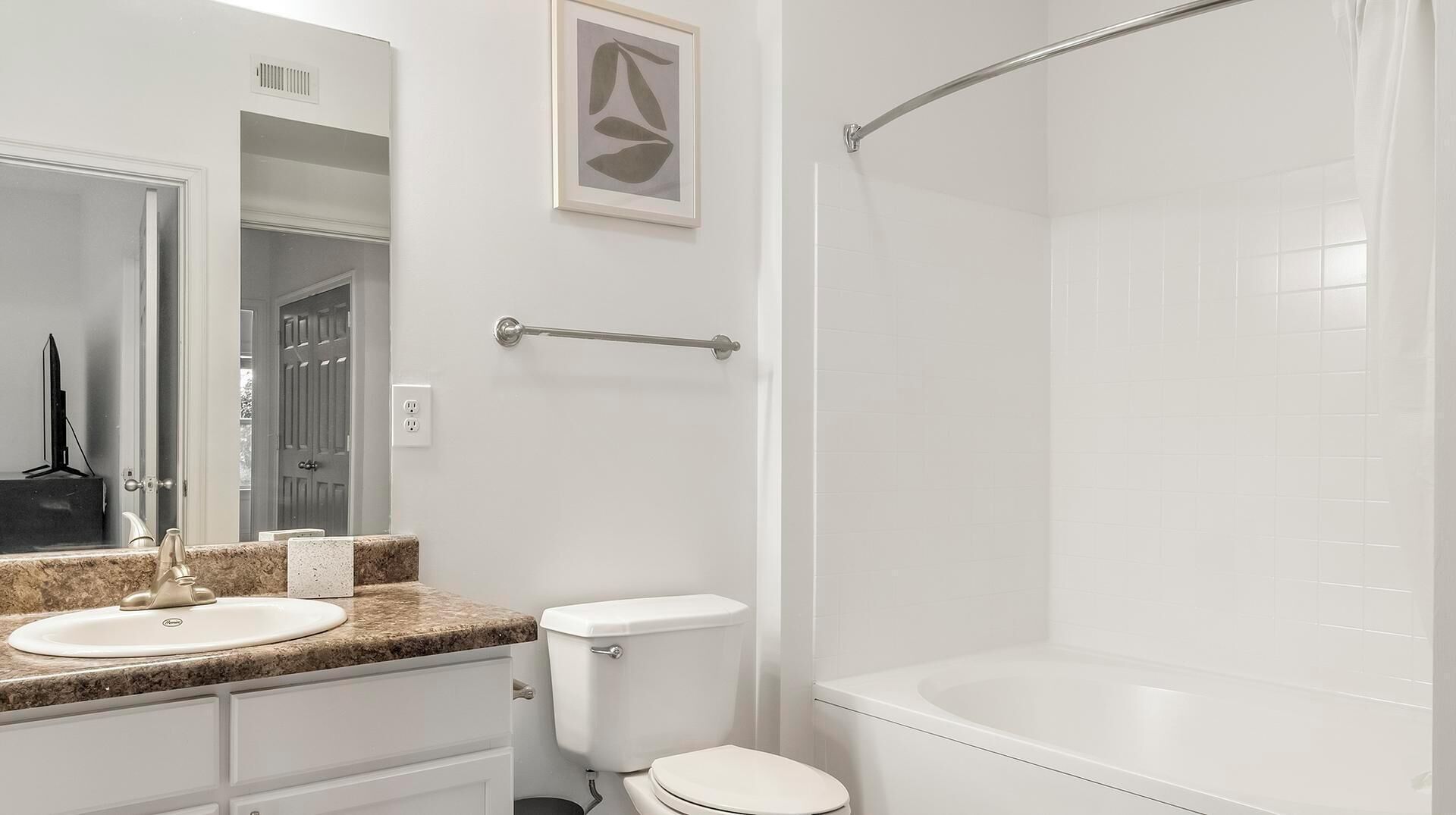A bathroom with a white sink, toilet, and bathtub. There is a towel rack above the toilet and a framed artwork on the wall.