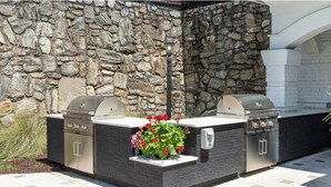 An outdoor kitchen with two grills and a built-in planter with flowers. - Landing | Stunning 2BD, Yoga Studio, Tennis Court (Atlanta)