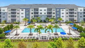 Un hotel de varios pisos con una piscina central rodeada de palmeras y sillas de descanso.
