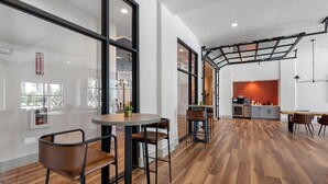 Un intérieur moderne avec un coin repas comprenant une table ronde et des chaises, une cuisine avec un mur de crédence rouge et une grande fenêtre à travers laquelle on peut voir un extincteur.