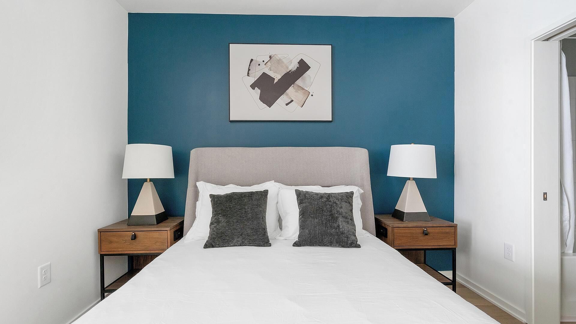 A bedroom with a bed, two bedside tables, and a wall-mounted abstract painting.