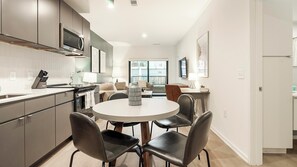 Een moderne keuken met een eethoek, met een ronde tafel en vier stoelen, een ingebouwde oven en een groot raam met uitzicht op de stad.