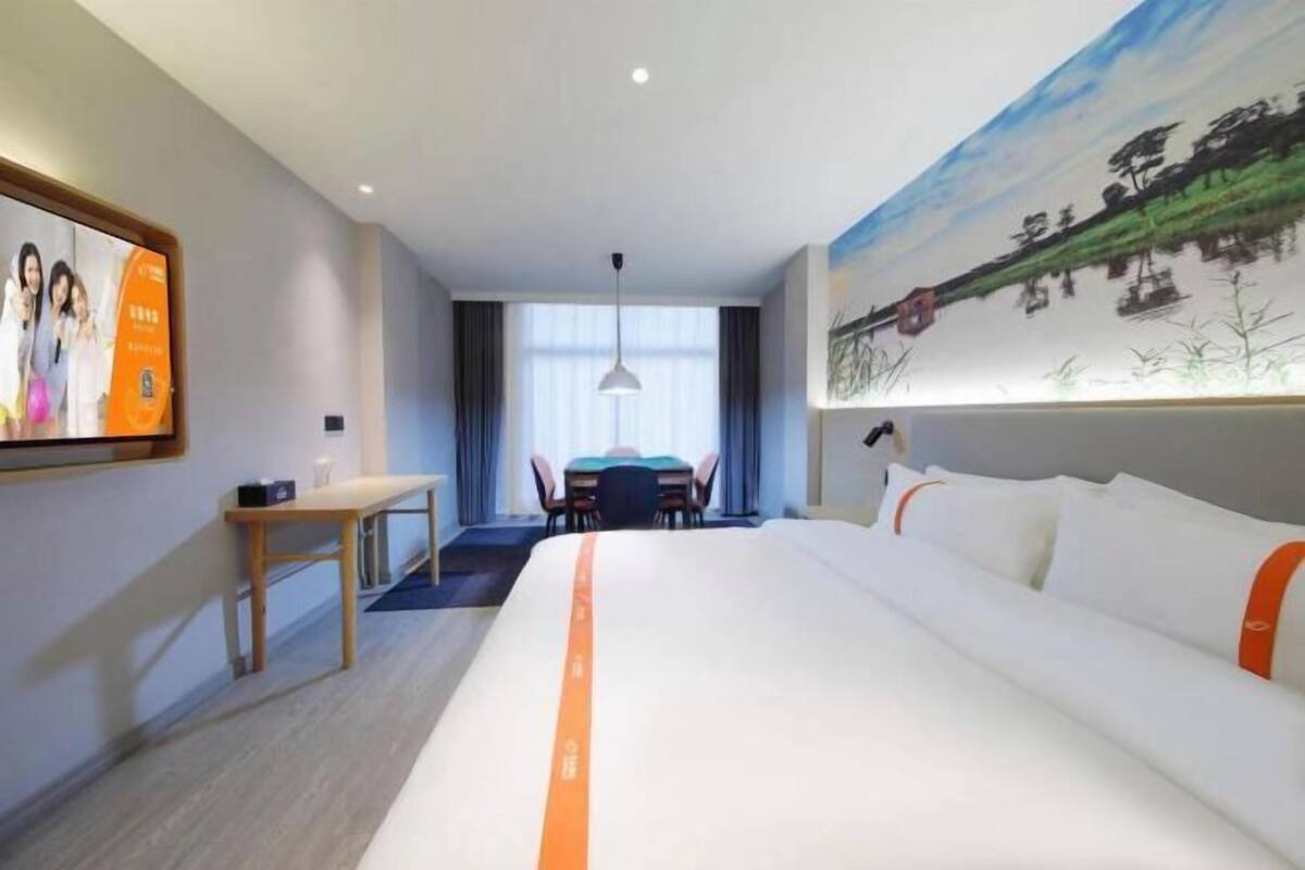 A hotel room with a large bed, a desk, a chair, a table, and a painting on the wall.