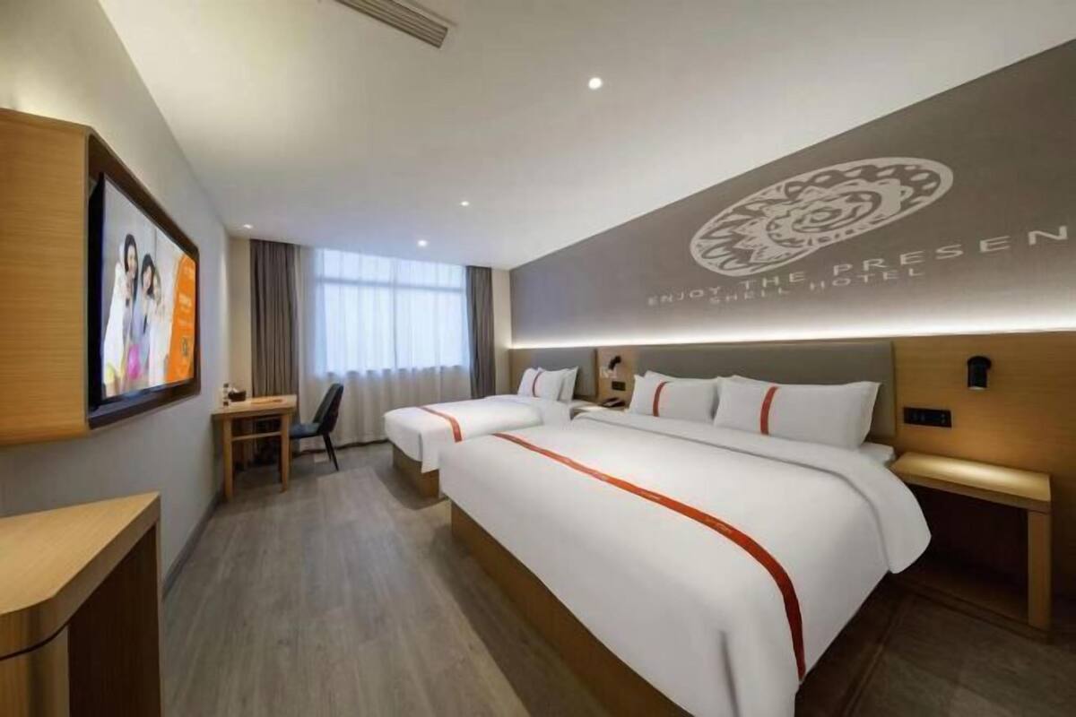 A hotel room with two beds, a desk, a chair, and a large window with curtains.