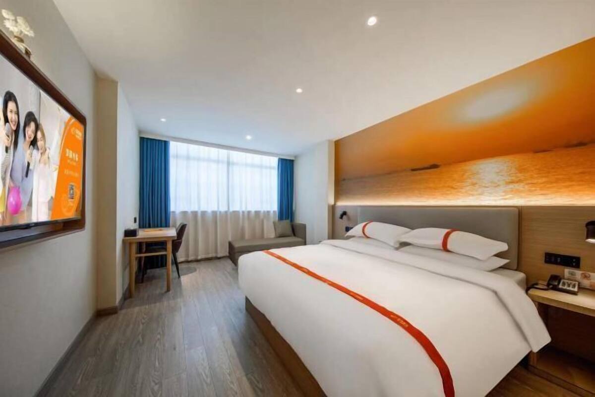 A hotel room with a bed, a desk, a chair, a TV, and a view of the sea.