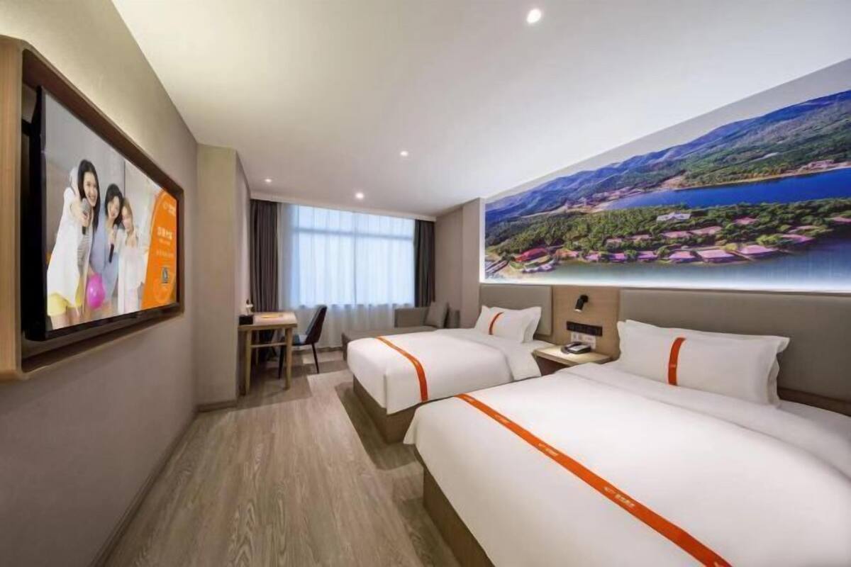 A hotel room with two beds, a desk, a chair, and a large window.