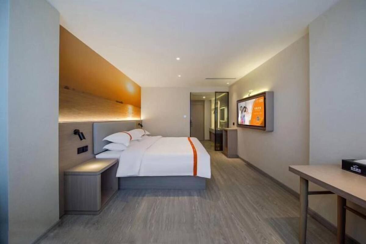 A modern hotel room with a bed, bedside tables, a desk, and a television.