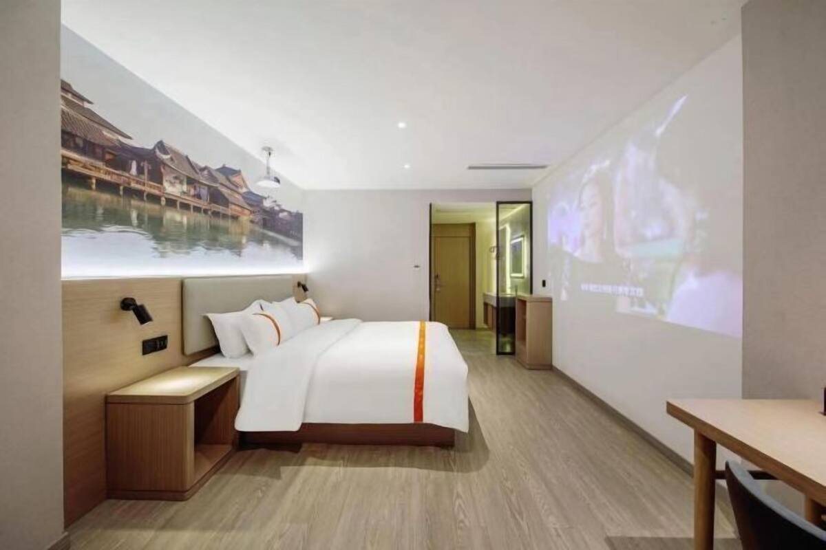 A modern hotel room with a bed, bedside table, and a projection screen displaying a scenic image.