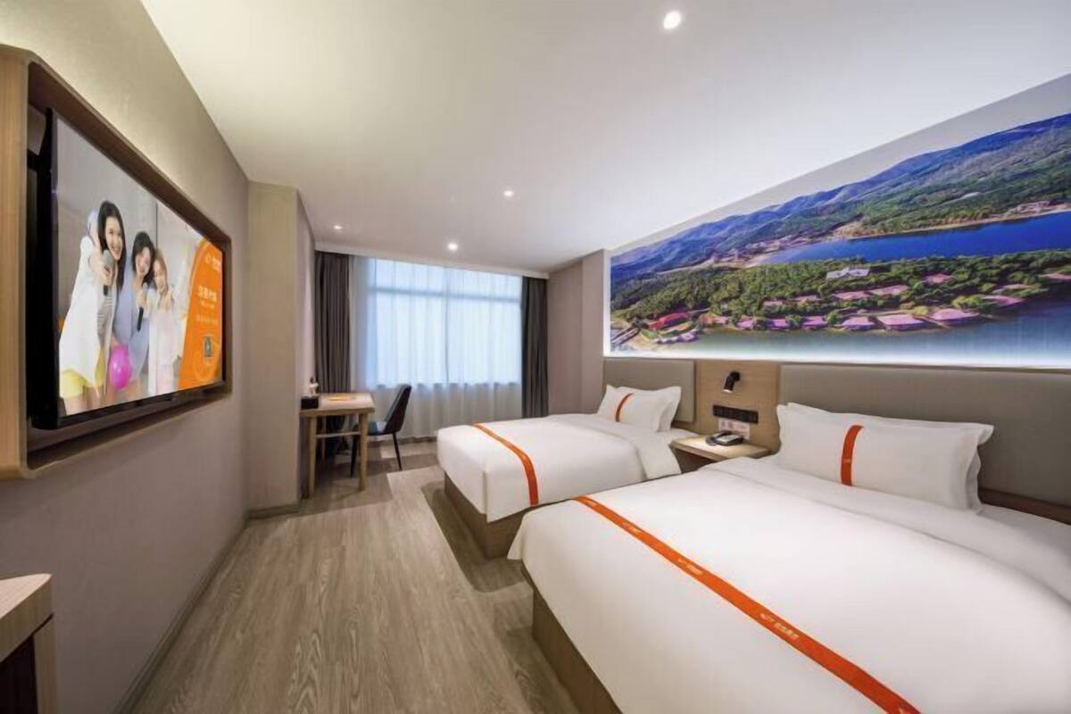 A hotel room with two beds, a desk, a chair, and a large window with a scenic view.