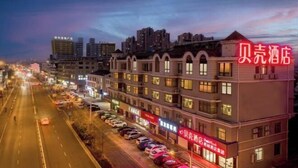 Un hôtel à plusieurs étages, une rangée de voitures garées devant et une enseigne lumineuse.