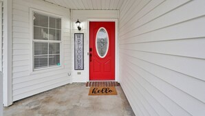 Ein Hauseingang mit roter Tür, einem 'WELCOME'-Schild und einer Fußmatte mit der Aufschrift 'hello'.