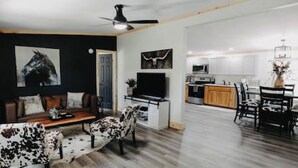 Een moderne woonkamer met een bank, een salontafel en een televisie. Er is een keuken met een magnetron en kastjes.