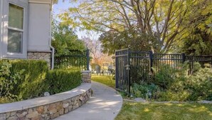Una propiedad residencial con un muro de contención de piedra, un camino de entrada pavimentado y una reja de metal negro.
